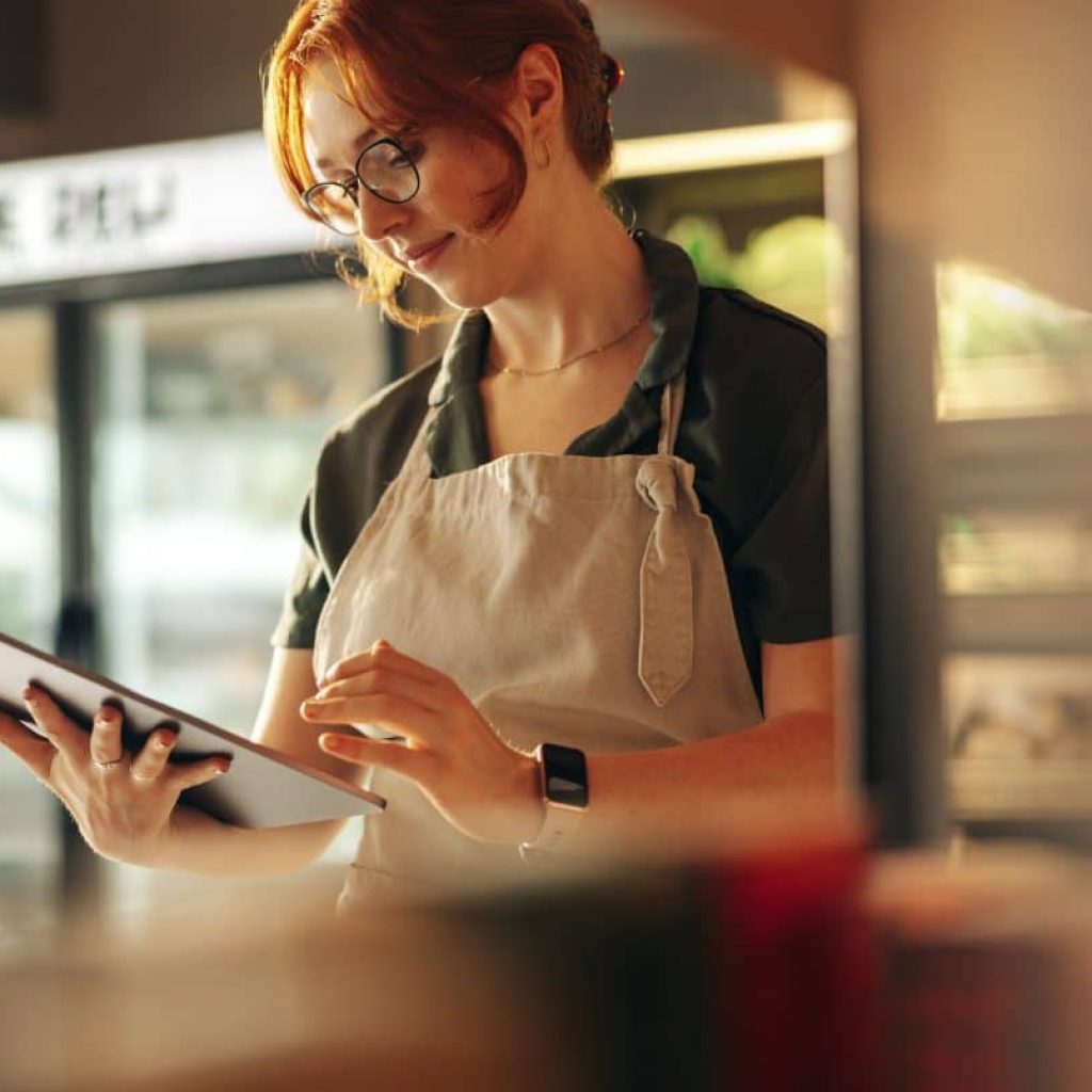 Cheerful shop owner using a digital tablet while standing in her grocery store. Successful female entrepreneur running her small business using wireless technology.