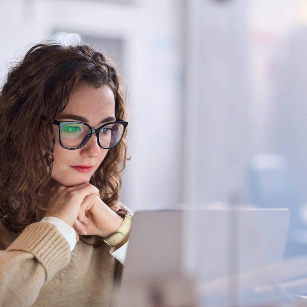 Young serious busy professional business woman employee or student wearing glasses using laptop watching online webinar or training web course, looking at computer, thinking, doing research.